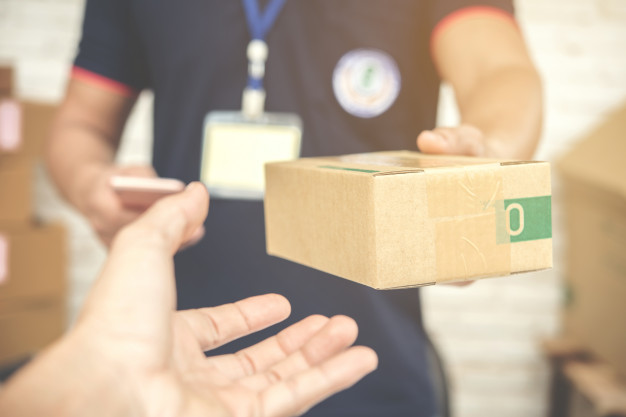 "Delivery man smiling and holding a cardboard box Free Photo"