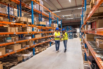 Two warehouse workers walking in distribution storage area discussing about logistics and organization
